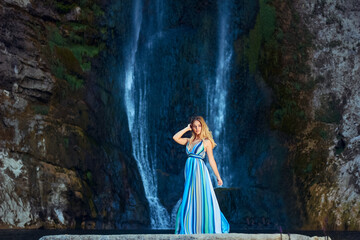 Young beauty in a long dress on the background of the Bliha waterfall