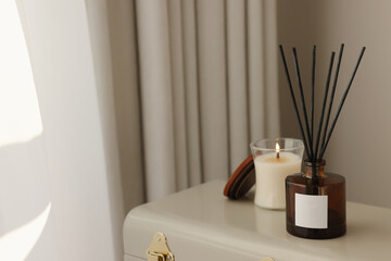 Aromatic reed air freshener and candle on suitcase indoors, space for text