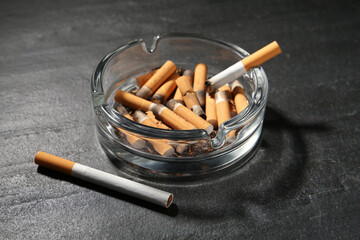 Glass ashtray with cigarette stubs on dark grey table