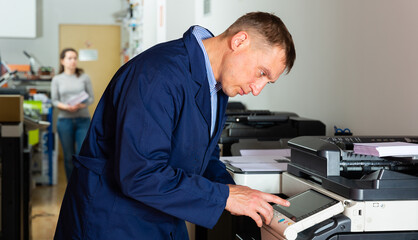 Portrait of confident service engineer standing by photocopy machine in office. High quality photo