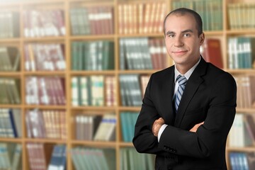 Mature professor standing with arms crossed in a library and posing