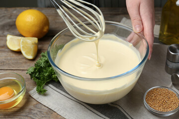 Woman making homemade mayonnaise in glass bowl at wooden table, closeup