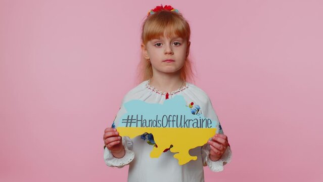 Portrait of Ukrainian girl child in embroidery dress showing banner with massage inscription text on map Hands Off Ukraine. Asking for help. Crisis, war, no peace, stop aggression from Russia country