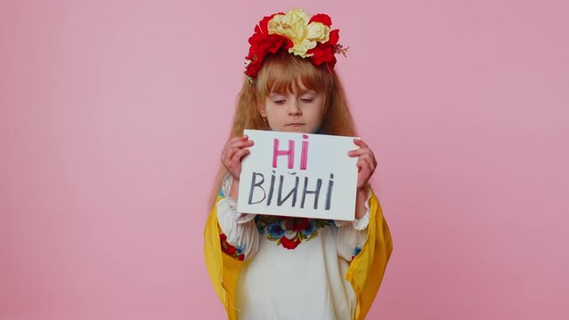 Ukrainian translation: No War. Schoolgirl toddler kid in embroidery dress holding banner with inscription massage, protesting war conflict in Ukraine. Crisis no peace. Child against Russian aggression