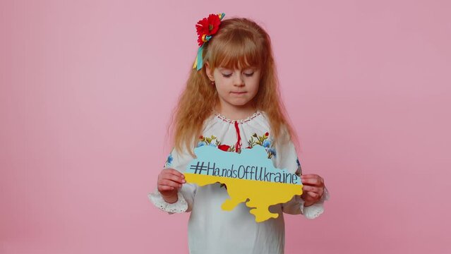 Angry toddler Ukrainian girl kid in embroidery dress protesting war conflict raises banner with inscription massage text on map Hands Off Ukraine on pink background. Peace, no war, stop aggression