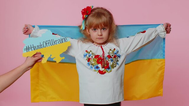 Upset toddler Ukrainian girl in embroidery dress protesting war conflict raises national flag. Inscription massage on map appears near kid with text Hands Off Ukraine. Peace, no war, stop aggression