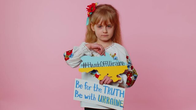Portrait of Ukrainian girl child in embroidery dress showing banner with massage inscription text on map Hands Off Ukraine. Asking for help. Crisis, war, no peace, stop aggression from Russia country