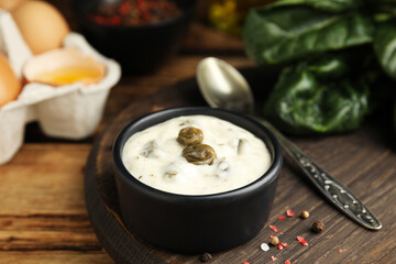 Caper sauce in bowl on wooden table, closeup