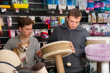 Father with teenager son and little dog choose products for cats in petshop. High quality photo
