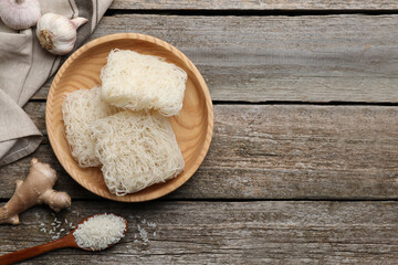 Bowl with dried rice noodles and ingredients on wooden table, flat lay. Space for text