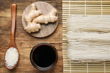 Flat lay composition with uncooked rice noodles, soy sauce and ginger on wooden table