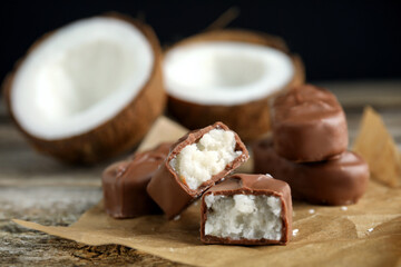 Delicious milk chocolate candy bars with coconut filling on wooden table, closeup. Space for text