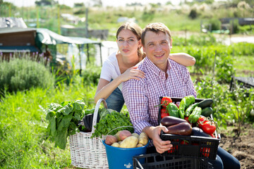 Happy family of gardeners posing with harvest of vegetables and greens in garden