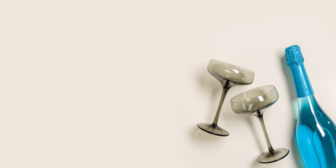 Champagne glasses tinted grey glass, Blue Champagne or blue sparkling wine bottle. Light Festive drink concept, glare and sunlight. Modern wine colored glasses. Wide banner