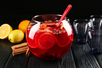 Bowl of delicious aromatic punch drink, ingredients and empty glasses on black wooden table