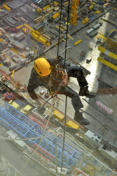 Skyscraper window cleaner hanging from a harness in Doha, Qatar. View from inside of the building behind a curtain of splashing water over the glass. 