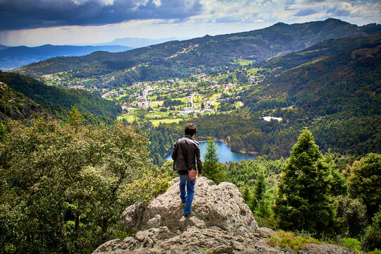 hombre parado en una roca frente a un abisco con  un paisaje y una ciudad en frente y un cielo nublado como el caminante sobre un mar de nubes