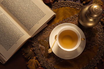 Toma cenital de taza de té de porcelana con cucharita dorada, mantel bordado y lectura de...