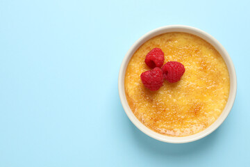 Delicious creme brulee with fresh raspberries on light blue background, top view. Space for text