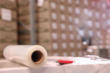 Roll of stretch film and utility knife on wrapped boxes in warehouse