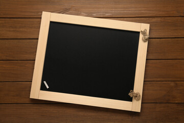 Clean blackboard with piece of white chalk on wooden table, top view