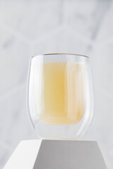 Healthy bone broth in a transparent mug on a pedestal on a light background.