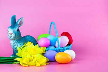 basket with easter eggs flowers and a rabbit on a pink background