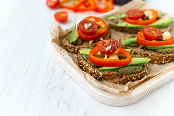 Dietary vegetarian sandwiches with cereal bread, vegetables and spicy sauce on a wooden plate on a white table. healthy eating. Side view, close-up, space for text.