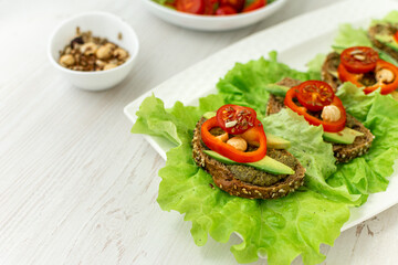 Vegan breakfast. Dietary nutrition. Sandwiches of grain bread with vegetables and nuts on a white plate on a white wooden table. Side view, close-up, space for text.