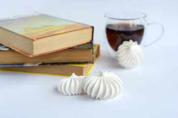 White airy meringue tea cookies in a glass cup and books on a light background