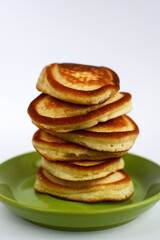 Delicious pancakes lie on top of each other on a green plate. Light background