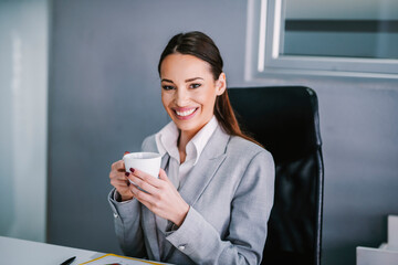 A businesswoman taking a break with cup of coffee at modern office and smiling at the camera.