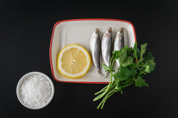 Salted sprat with parsley and lemon on a black table. Flat lay.