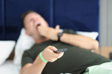 Yawning man is holding remote control closeup