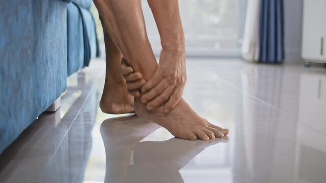 Patient mature woman with arthritis sitting on bed and rubbing his ankle and foot relieving the ache,Tracking shot