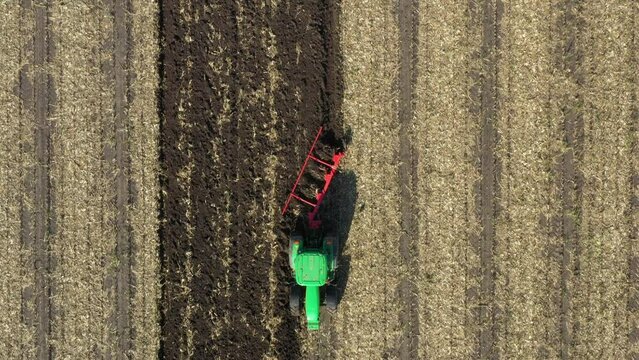 Aerial top view in dolly moving shot of tractor as plowing the ground on cultivated farm field, preparing soil for planting new crop next season.