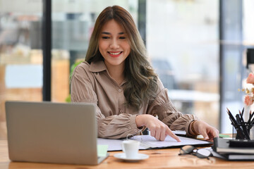 Obraz premium Charming businesswoman working at the laptop and reading documents at office desk.