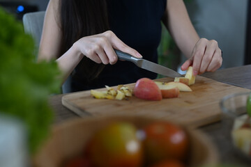 Young woman preparing vegan salad with fresh vegetables and fruits in the kitchen at home.