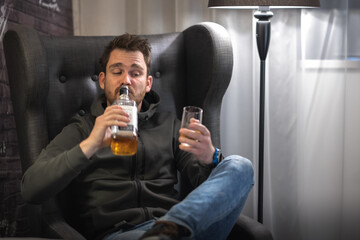 Young drunk is drinking whiskey from bottle, not using a glass. Alcohol abuse, young male heavy drinking whisky in a room