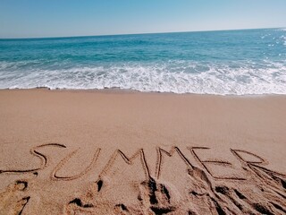 Summer written in the sand on the beach at the edge of the shore.