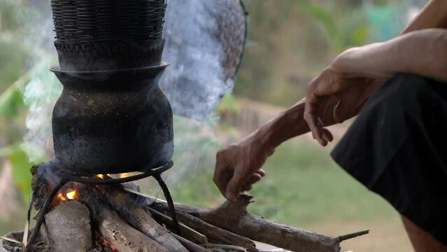 Close up, Hands of Senior man with firewood to burn in stove to steamed sticky rice with, The simble life of the rural people in Thailand