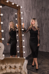 Portrait of beautiful sexy blonde woman in black dress and in loft near big mirrors, looking to the mirror.