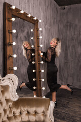 Portrait of beautiful sexy blonde woman in black dress and in loft near big mirrors, looking to the camera.