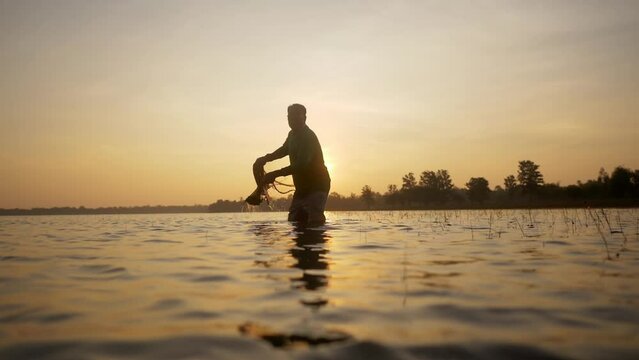 Slow motion shot, Silhouette Asian Senior Fisherman wearing eyeglasses standing in water and fishing net to fishing at river in early morning