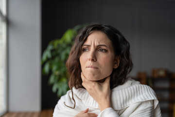 Young sick worried woman with sore throat at home touching neck, unhealthy female wrapped in plaid having swollen lymph nodes caused by bacterial infection, feeling pain or discomfort while swallowing - obrazy, fototapety, plakaty