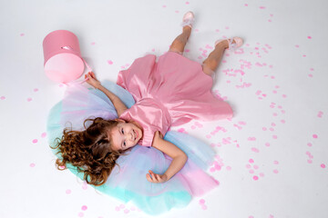 Obraz na płótnie Canvas beautiful little girl in a chic pink dress lies on the floor strewn with confetti. top view. fashion and style. child celebrates his birthday. photo in the studio. space for text. High quality photo
