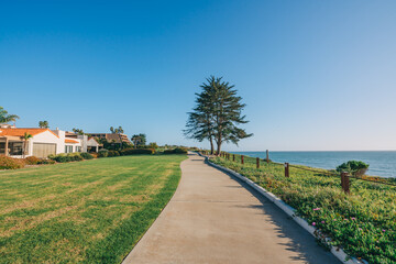 Long walkway along the shore, houses with nicely  landscaped front the yard and clear blue sky on background in a small beach town, California