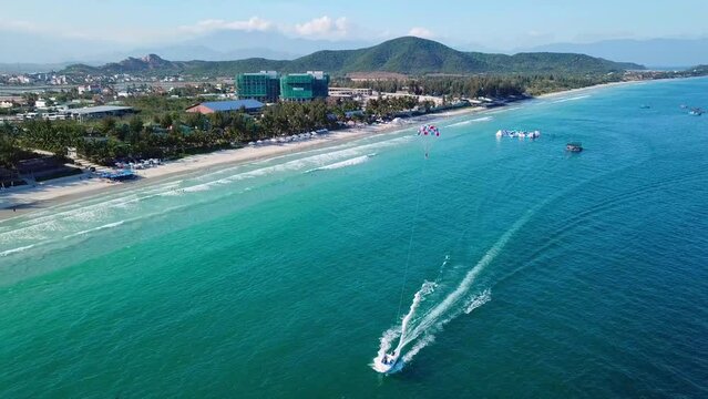 Tourists parasailing over sea coastline, drone point view. Aerial footage of people on parachute above tropical beach.
