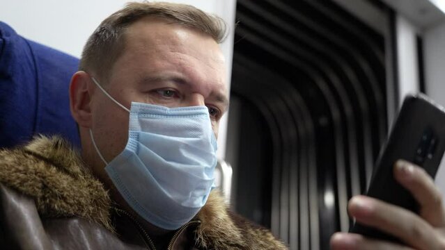 Disgusted and overwhelmed cringe millennial man stares at screen of smart phone while riding home by train passes through suburbs during Covid-19 or coronavirus pandemiс, new normal