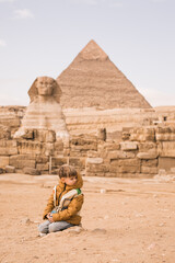 Fototapeta na wymiar little boy sitting on knees at background of Great Sphinx and Chephren's pyramid in Giza, Egypt